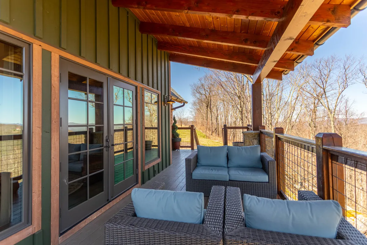 A serene outdoor seating area under a covered section of the deck, framed by sturdy wooden beams and surrounded by lush natural foliage. The view looks out onto the ever-changing forest, emphasizing the four-season appeal and tranquil atmosphere.