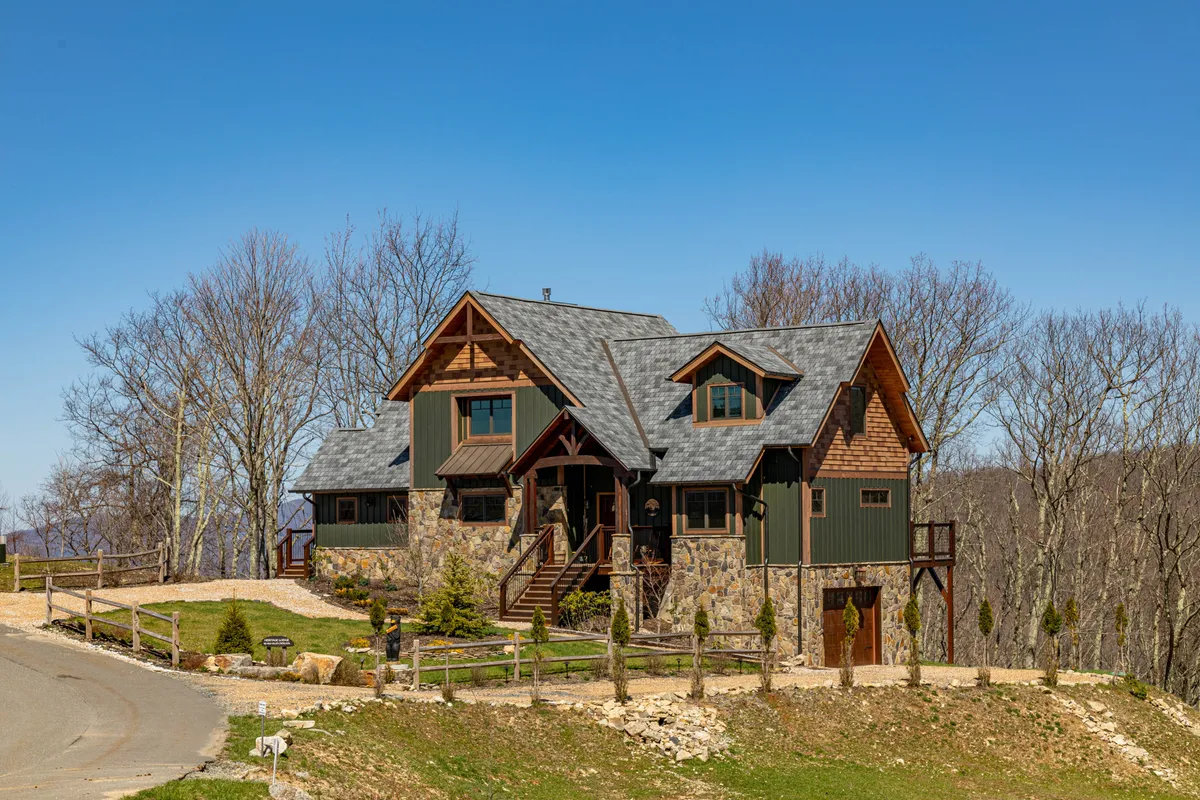 The image displays the welcoming stone facade and gabled roof of a home at Eagles Nest, with a spacious front porch set amid lush greenery. The inviting outdoor area is perfect for family gatherings, barbecues, or simply relaxing and enjoying the mountain air, connecting the private home setting with the broader community amenities.