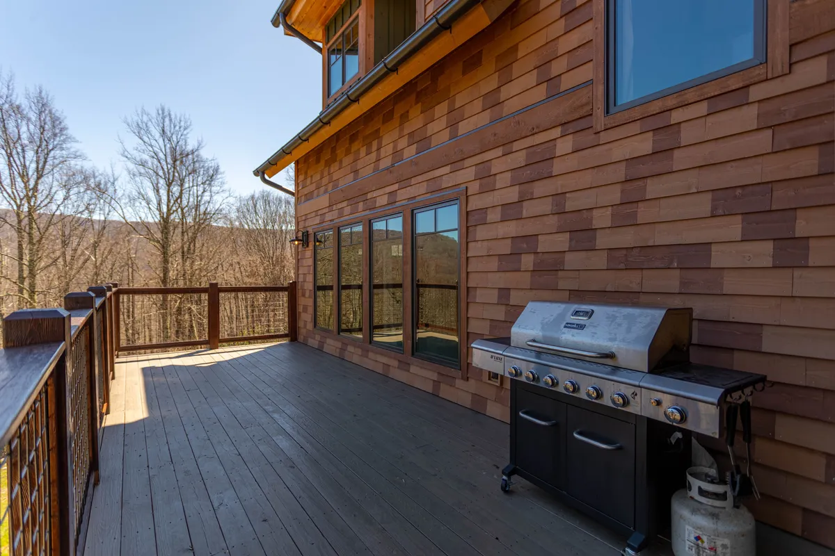 A wooden deck with a grill, outdoor dining area, and unobstructed mountain views. The relaxed atmosphere invites guests to unwind after a day of adventure, with the mountains stretching out under a colorful sky.