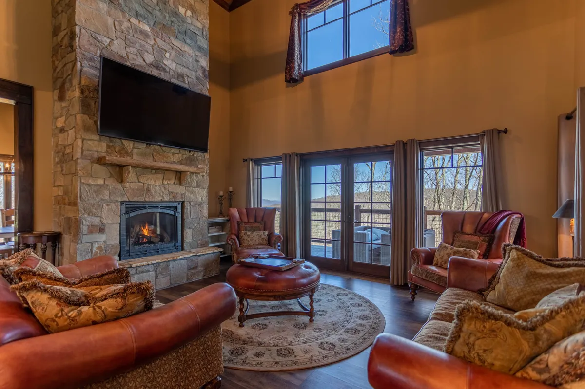 This image captures a cozy living room with a prominent stone fireplace, large windows revealing the mountain landscape, and luxurious plush seating arranged for relaxation and conversation. The atmosphere is warm and inviting, ideal for gatherings or unwinding after a day outdoors.