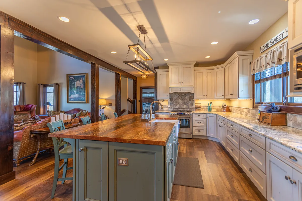 A spacious kitchen featuring a large central island with bar seating, gleaming stainless steel appliances, granite countertops, and rustic wooden beams overhead. The open layout allows for seamless interaction with adjacent spaces, inviting both cooking and conversation.