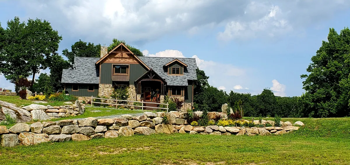 This image features the exterior of Heritage Lodge, showcasing the welcoming house, a classic stone wall, and a beautifully landscaped garden. The inviting porch and surrounding yard emphasize the connection to the natural mountain setting.