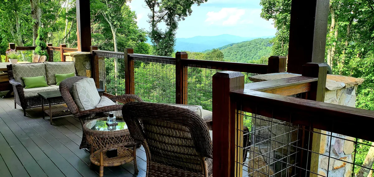 A closer look at a cozy seating arrangement on the deck, set against a lush green backdrop and distant peaks. The scene evokes gatherings at sunrise or twilight, with a clear emphasis on the peaceful ambience and opportunities for socializing or quiet reflection.