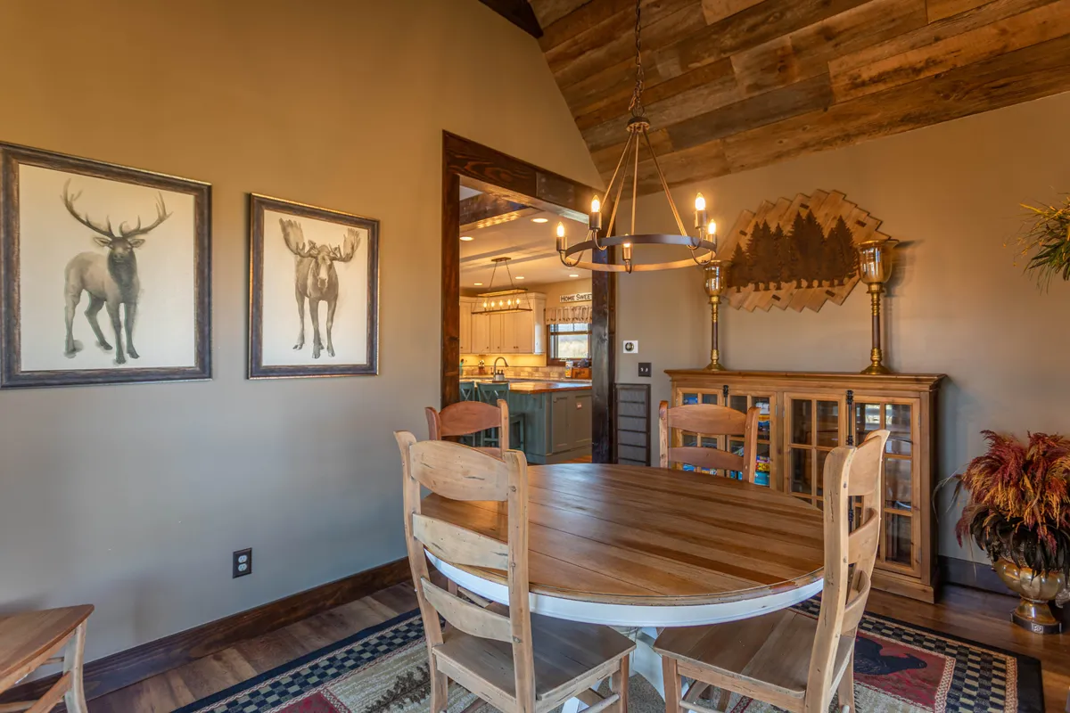 A warm dining area with a wooden table, chandelier, framed moose artwork, and inviting decor, set up for group meals and celebrations. The scene conveys a sense of joy and shared moments.