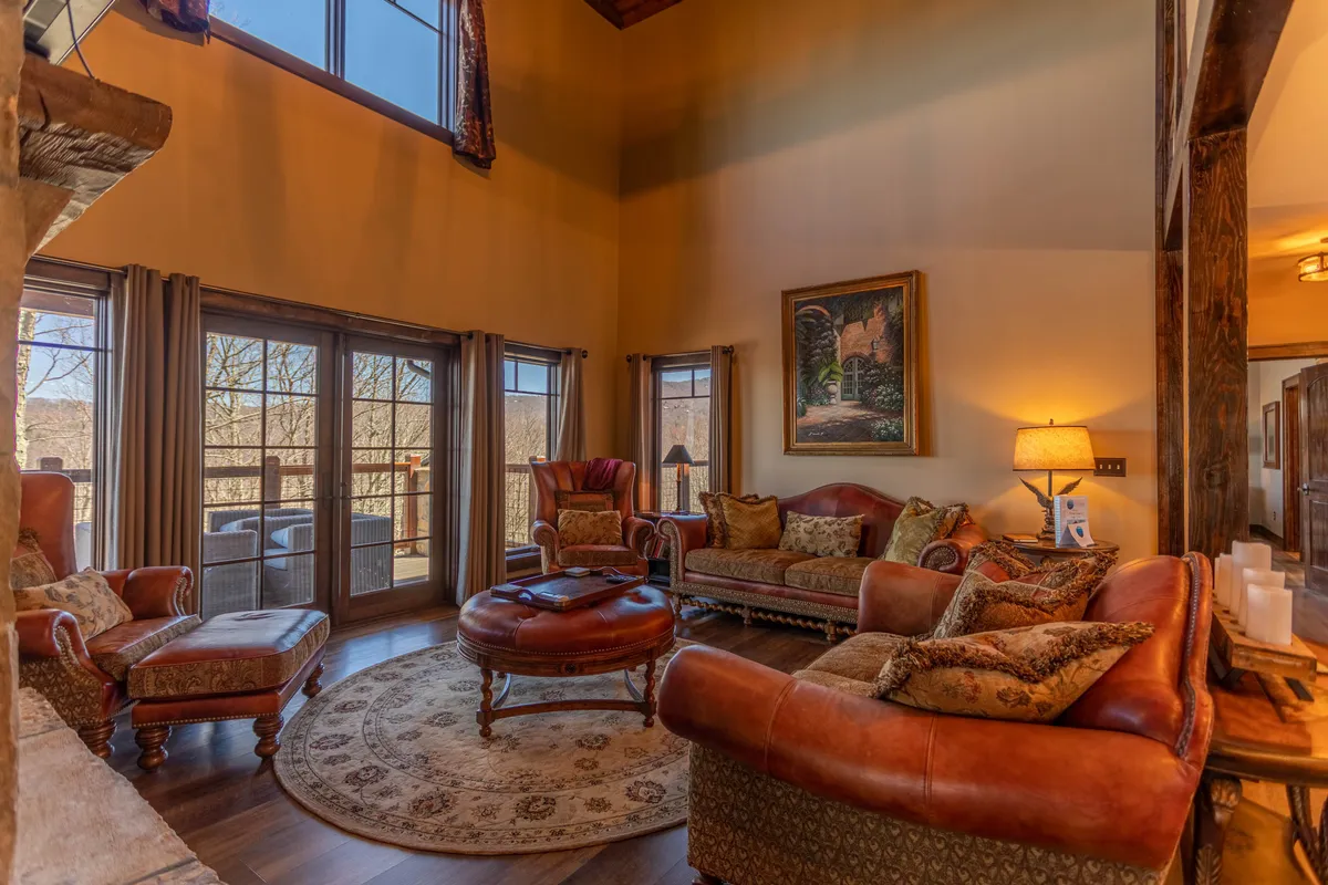 A spacious living room filled with natural light from large windows, offering comfortable seating arranged for socializing or relaxing. Decorative artwork and an intricate area rug add touches of style and warmth, and the room exudes a cozy, inviting atmosphere ideal for unwinding or hosting intimate gatherings.